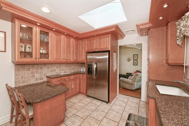 kitchen featuring a skylight, tasteful backsplash, sink, dark stone counters, and stainless steel fridge with ice dispenser