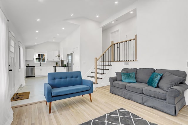 living area featuring baseboards, stairs, light wood-style floors, high vaulted ceiling, and recessed lighting