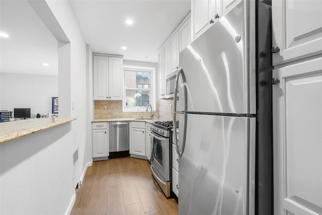 kitchen with sink, light hardwood / wood-style flooring, appliances with stainless steel finishes, white cabinets, and decorative backsplash