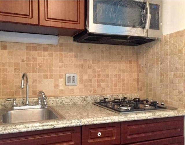 kitchen featuring light stone counters, stainless steel appliances, sink, and backsplash