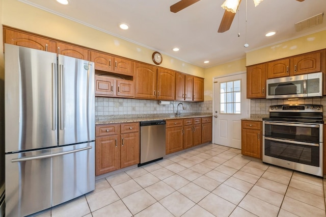 kitchen with light tile patterned flooring, appliances with stainless steel finishes, tasteful backsplash, sink, and light stone counters