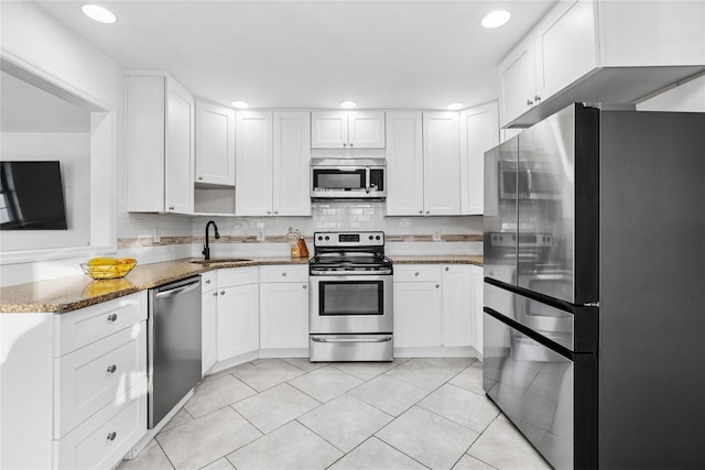 kitchen featuring appliances with stainless steel finishes, white cabinetry, sink, dark stone counters, and light tile patterned floors