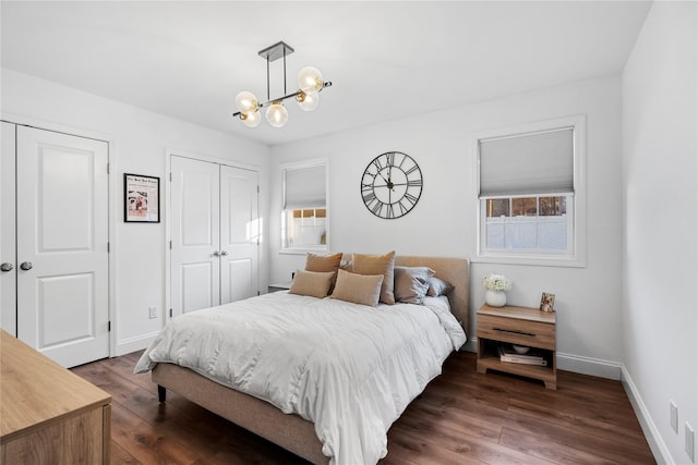 bedroom featuring dark wood-type flooring, multiple closets, a chandelier, and multiple windows