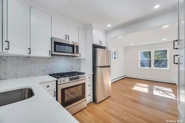 kitchen with light hardwood / wood-style flooring, baseboard heating, appliances with stainless steel finishes, decorative backsplash, and white cabinets