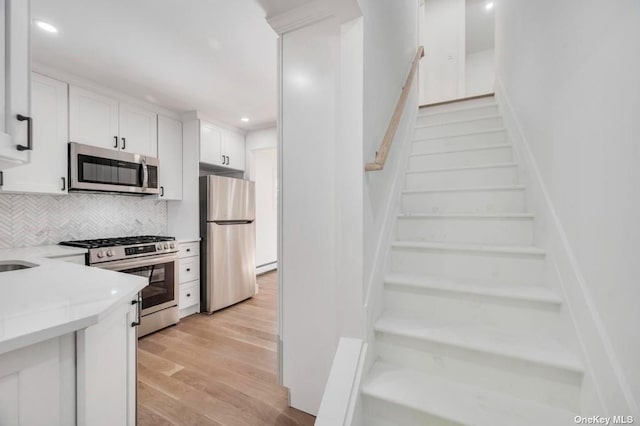 kitchen featuring stainless steel appliances, light hardwood / wood-style flooring, white cabinets, and decorative backsplash