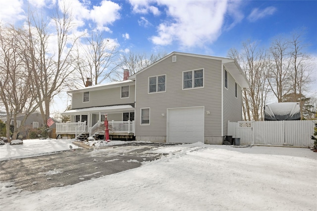 snow covered rear of property with a garage, a chimney, and fence