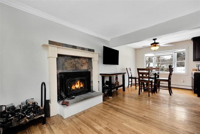 living room featuring light hardwood / wood-style flooring, ornamental molding, ceiling fan, a tiled fireplace, and a baseboard heating unit