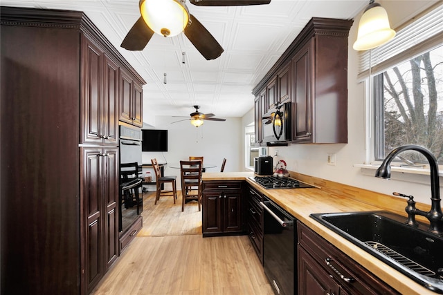 kitchen with butcher block countertops, sink, light wood-type flooring, ceiling fan, and black appliances