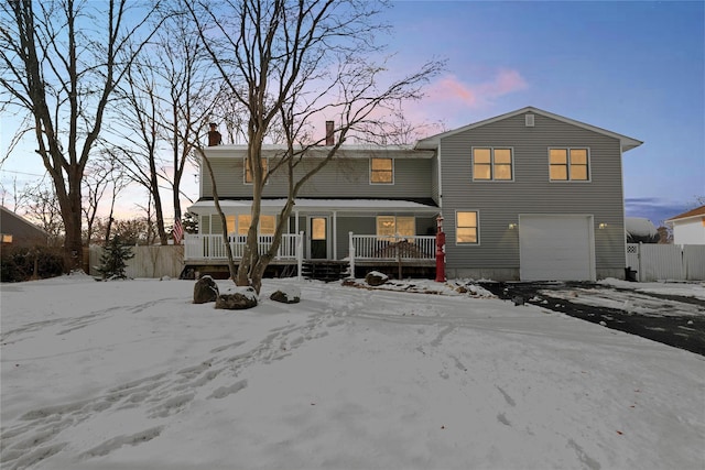 snow covered back of property with a garage, a chimney, fence, and a porch