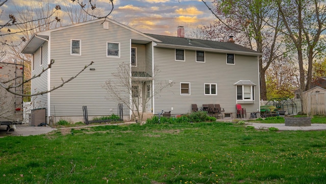 4 Young Rd, Coram, NY 11727 - back of house at dusk with a chimney, a storage unit, a patio, and a lawn