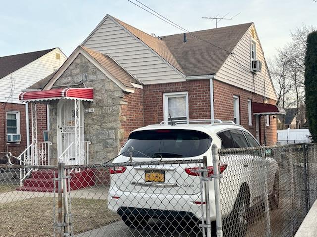 bungalow-style home featuring a fenced front yard, cooling unit, brick siding, roof with shingles, and a gate