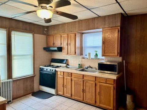 221-14 114th Rd, Cambria Heights, NY 11411 - kitchen with range with gas stovetop, tile countertops, radiator heating unit, stainless steel microwave, and range hood