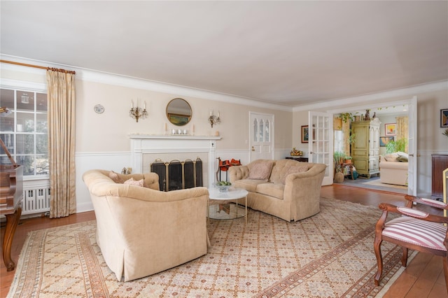 living area with a wainscoted wall, light wood-style flooring, a fireplace, and crown molding