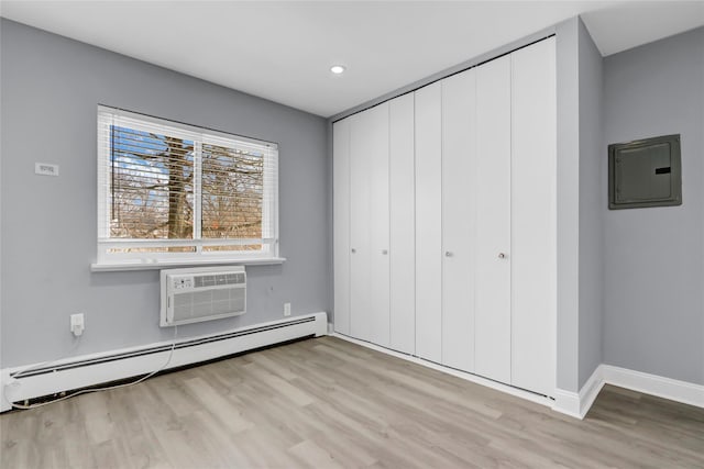 unfurnished bedroom with baseboard heating, electric panel, a wall mounted air conditioner, a closet, and light wood-type flooring