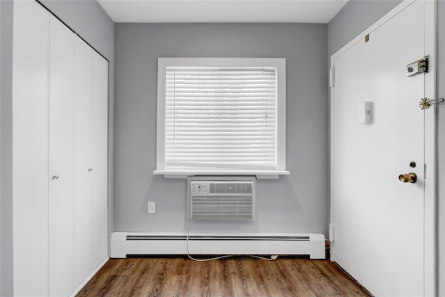 interior space featuring a wall mounted air conditioner, a baseboard radiator, and wood-type flooring