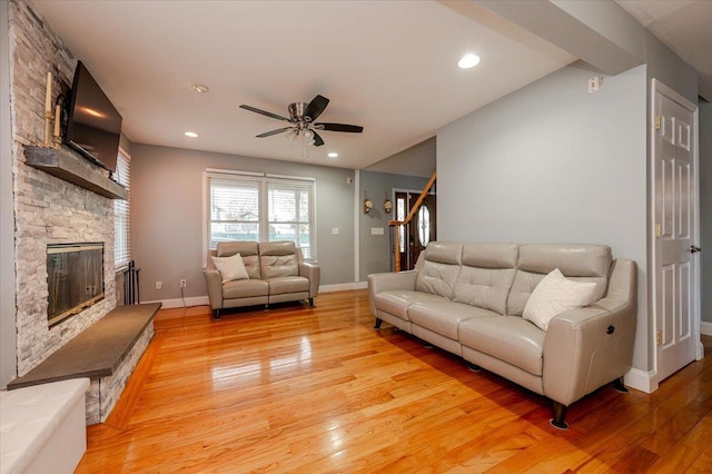 living room featuring ceiling fan, a stone fireplace, and light wood-type flooring