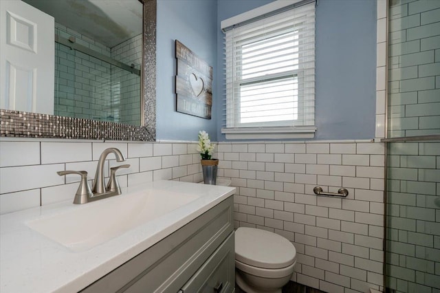 bathroom featuring vanity, toilet, a shower with shower door, and tile walls