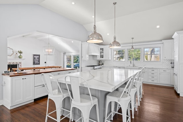 kitchen with premium range hood, vaulted ceiling, hanging light fixtures, and white cabinets