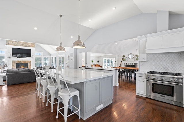 kitchen featuring pendant lighting, stainless steel stove, a fireplace, white cabinets, and light stone counters