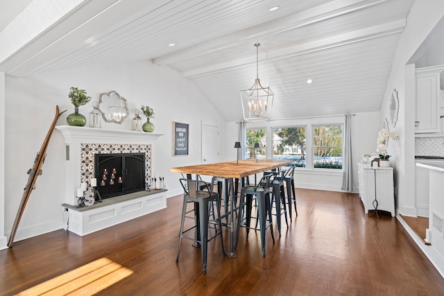 dining area with dark wood-type flooring, a tiled fireplace, an inviting chandelier, and vaulted ceiling with beams