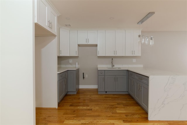 kitchen featuring sink, light wood-type flooring, gray cabinets, pendant lighting, and white cabinets