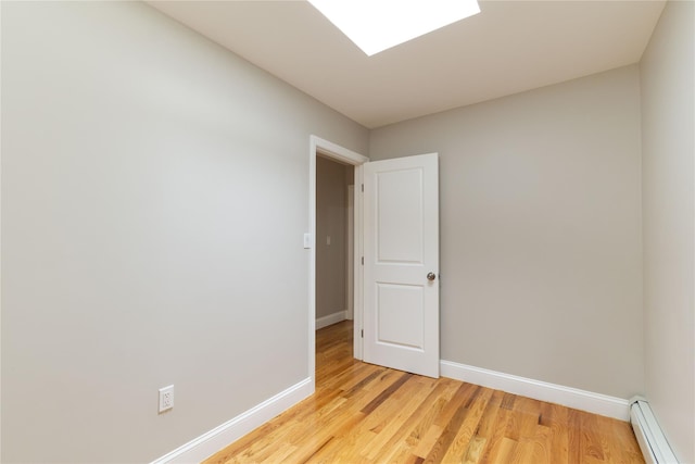 unfurnished room with a baseboard heating unit and light wood-type flooring