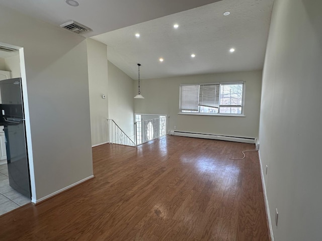 unfurnished living room with vaulted ceiling, light hardwood / wood-style flooring, and a baseboard heating unit