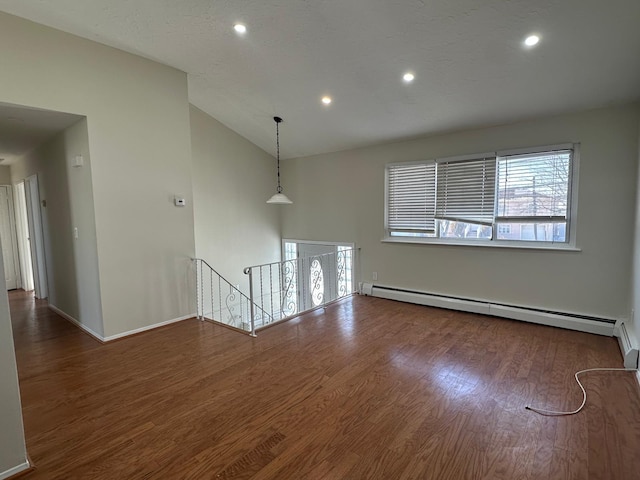 empty room featuring dark hardwood / wood-style flooring, vaulted ceiling, and a baseboard heating unit