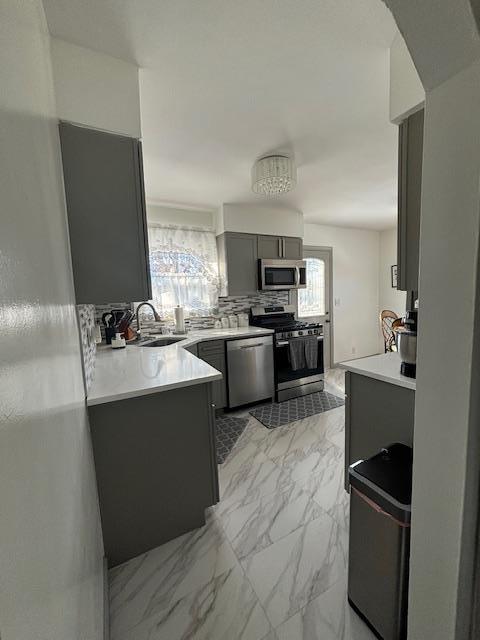 kitchen featuring sink, gray cabinetry, appliances with stainless steel finishes, kitchen peninsula, and backsplash