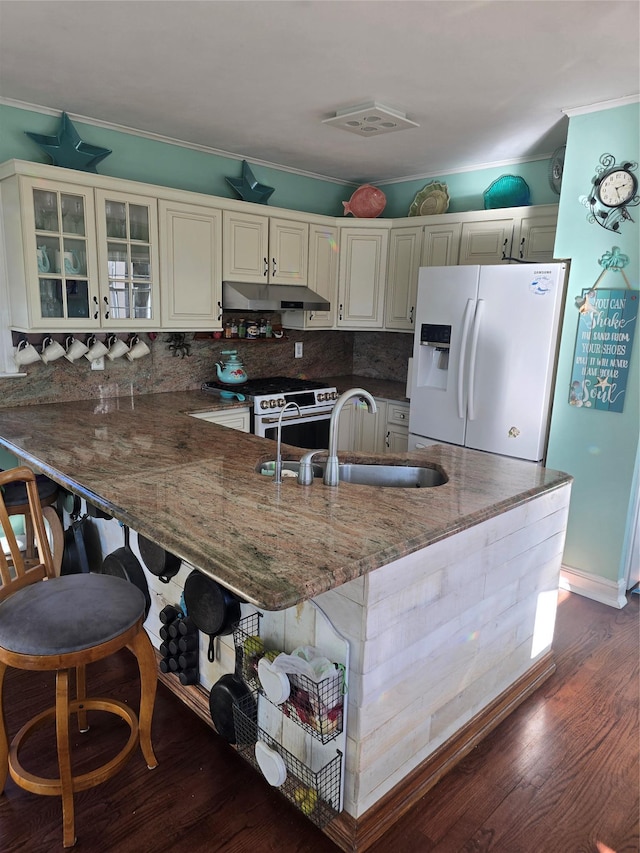 kitchen with white refrigerator with ice dispenser, ornamental molding, a sink, a peninsula, and under cabinet range hood