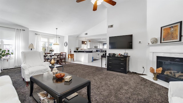 carpeted living room with ceiling fan and high vaulted ceiling