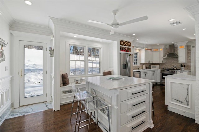 kitchen featuring wall chimney exhaust hood, white cabinetry, a center island, appliances with stainless steel finishes, and decorative backsplash