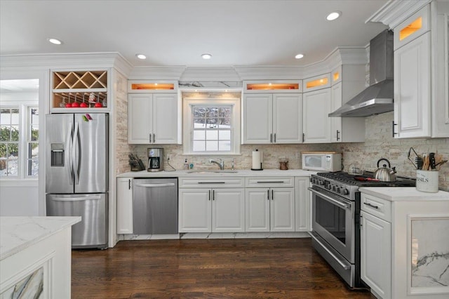 kitchen featuring stainless steel appliances, wall chimney range hood, white cabinets, and backsplash