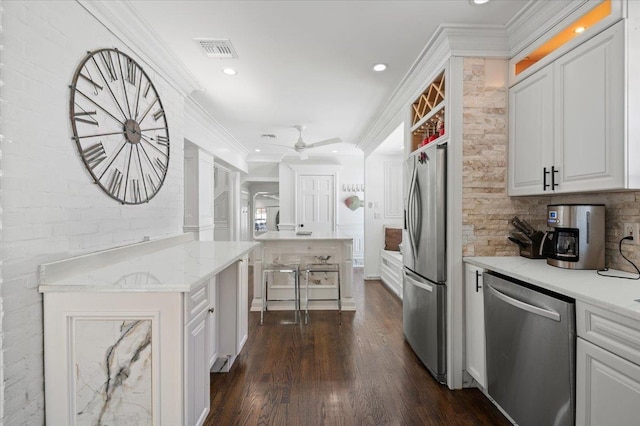 kitchen with light stone counters, tasteful backsplash, ornamental molding, appliances with stainless steel finishes, and white cabinets