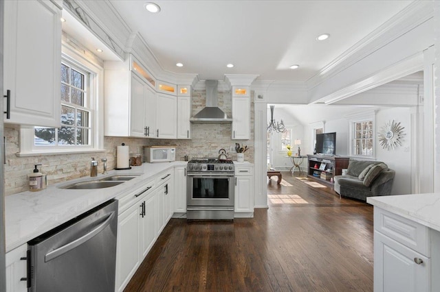 kitchen with white cabinets, appliances with stainless steel finishes, sink, and wall chimney range hood