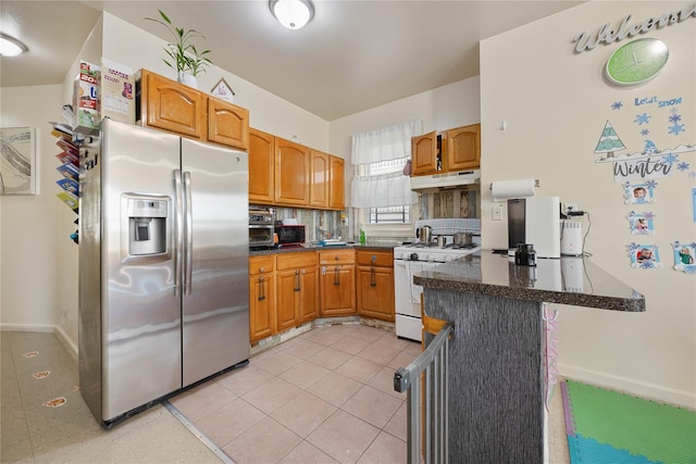 kitchen featuring stainless steel refrigerator with ice dispenser, light tile patterned flooring, white range with gas stovetop, and kitchen peninsula