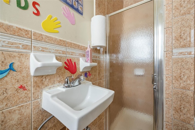 bathroom featuring a shower with door, sink, and tile walls