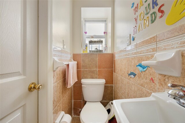 bathroom featuring toilet, sink, and tile walls