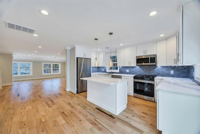 kitchen with light stone counters, decorative light fixtures, a kitchen island, stainless steel appliances, and white cabinets