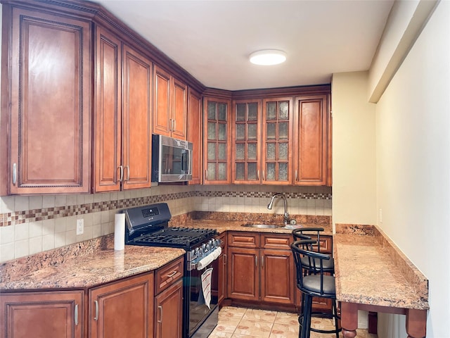 kitchen featuring sink, decorative backsplash, light tile patterned floors, light stone counters, and gas range oven