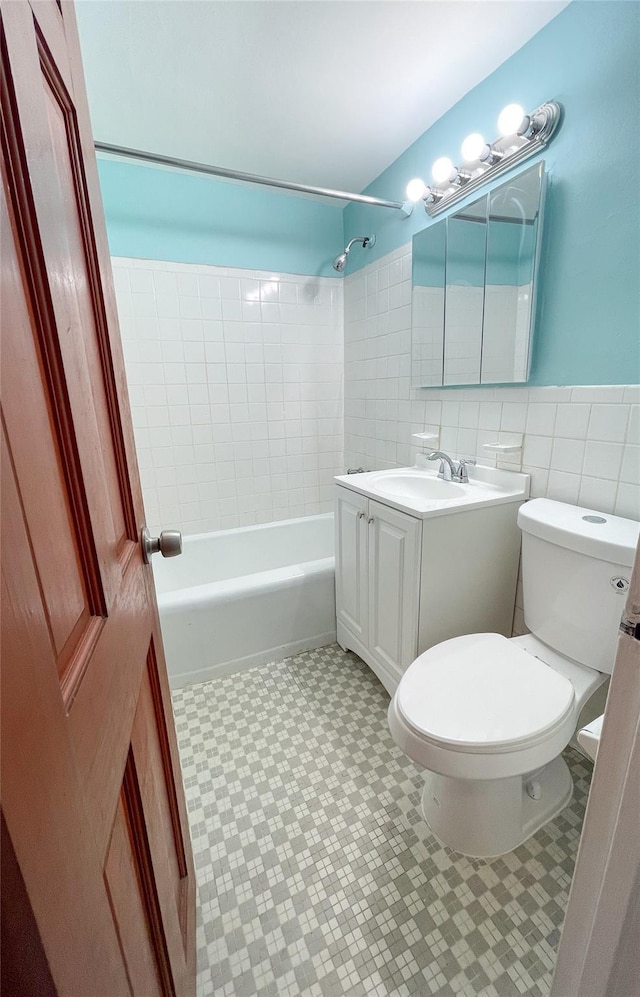 full bathroom featuring vanity, toilet, tiled shower / bath combo, and tile walls