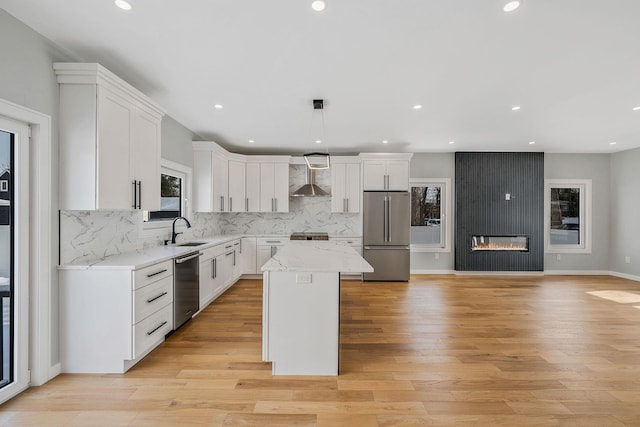 kitchen featuring wall chimney range hood, stainless steel fridge, white cabinets, a kitchen island, and decorative light fixtures