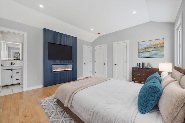 bedroom with lofted ceiling, two closets, a fireplace, and light hardwood / wood-style floors