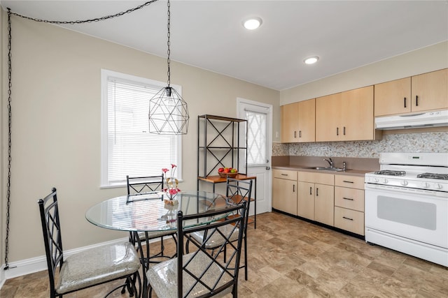 kitchen with under cabinet range hood, light brown cabinetry, pendant lighting, and white gas stove