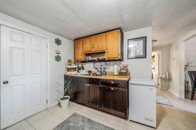 kitchen with sink, light tile patterned floors, a textured ceiling, and refrigerator