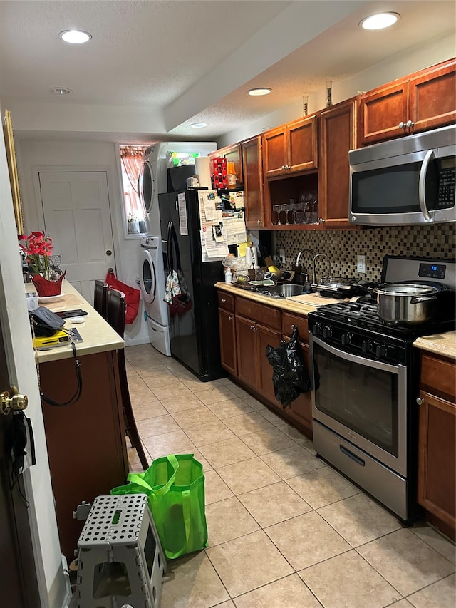 kitchen featuring stacked washer and clothes dryer, sink, light tile patterned floors, stainless steel appliances, and backsplash