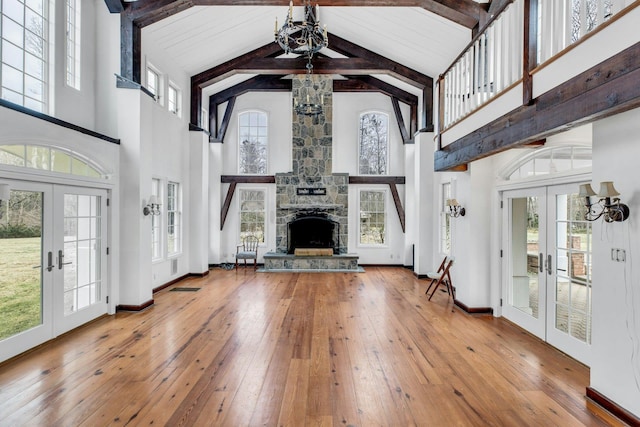 unfurnished living room with a stone fireplace, plenty of natural light, high vaulted ceiling, and french doors