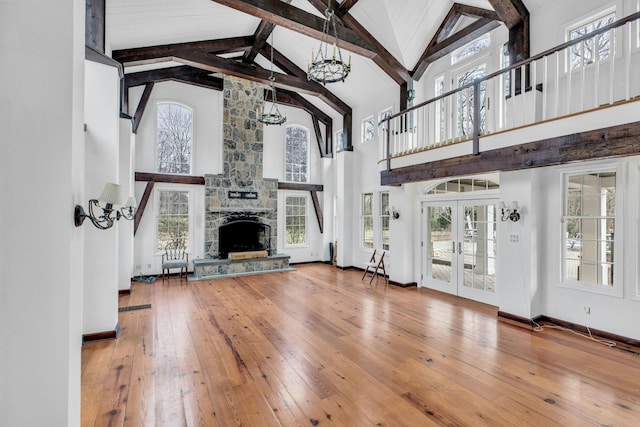 unfurnished living room featuring french doors, beam ceiling, wood-type flooring, high vaulted ceiling, and a fireplace