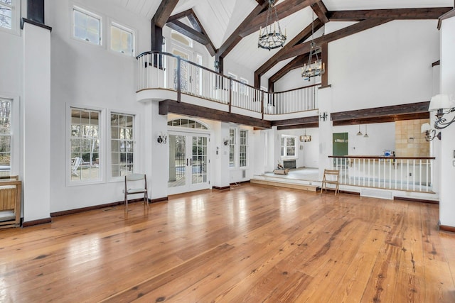 unfurnished living room featuring french doors, a chandelier, high vaulted ceiling, and hardwood / wood-style floors