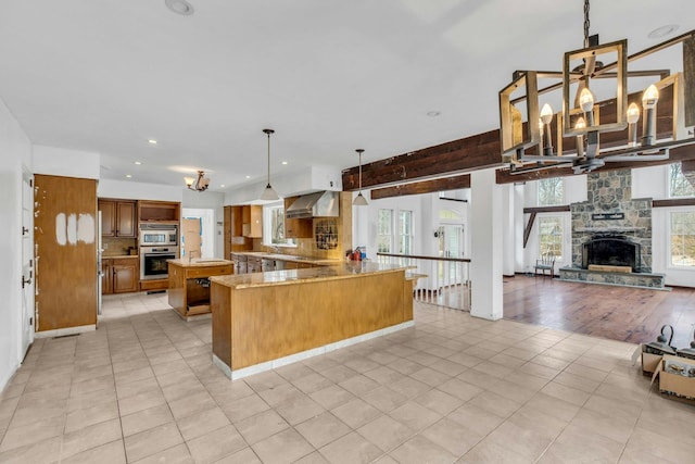 kitchen with pendant lighting, light tile patterned floors, kitchen peninsula, light stone countertops, and wall chimney exhaust hood